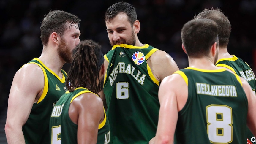 Andrew Bogut puts his dark green singlet in his mouth as teammates crowd around him