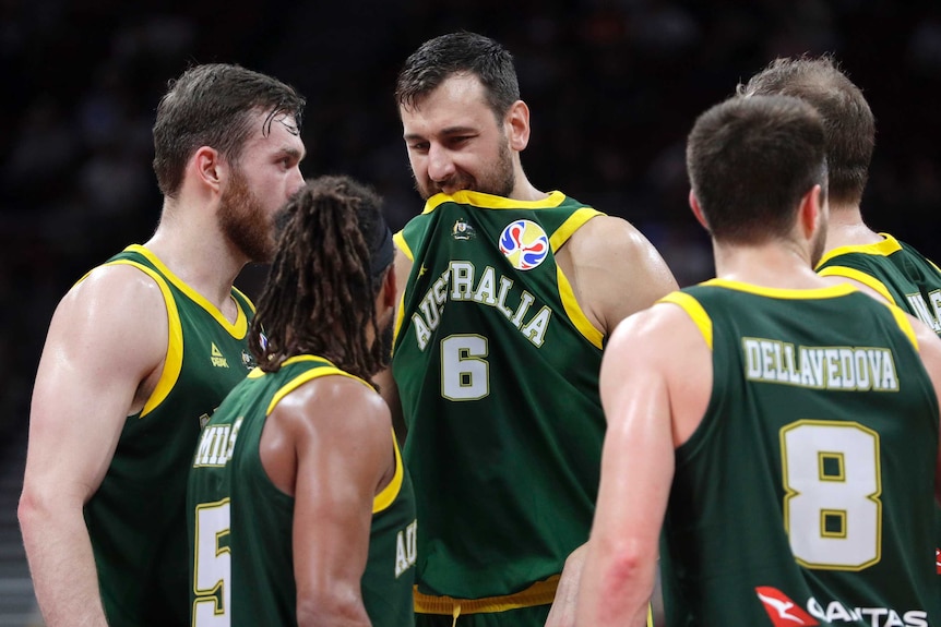 Andrew Bogut puts his dark green singlet in his mouth as teammates crowd around him