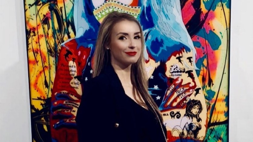 a blonde woman standing in front of a colourful painting