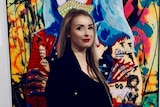 a blonde woman standing in front of a colourful painting