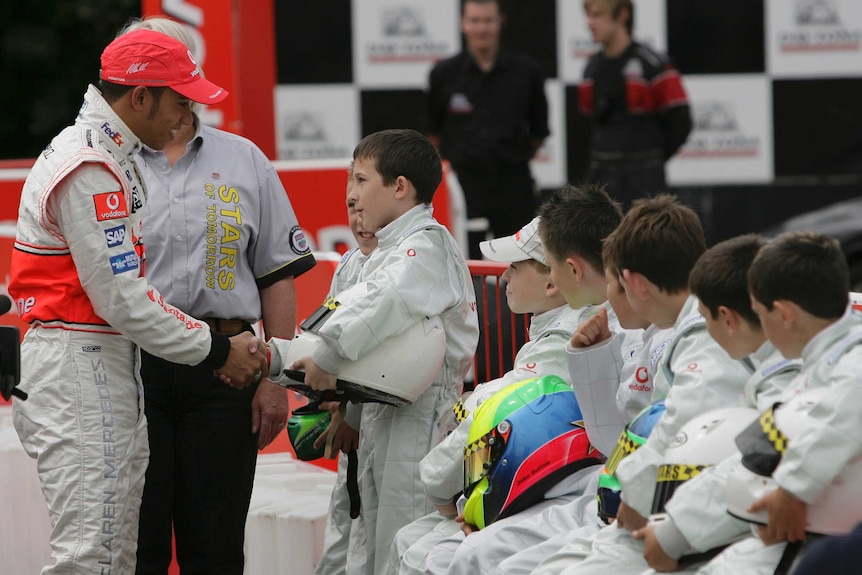 Lewis Hamilton shakes hands with a young racing car driver.