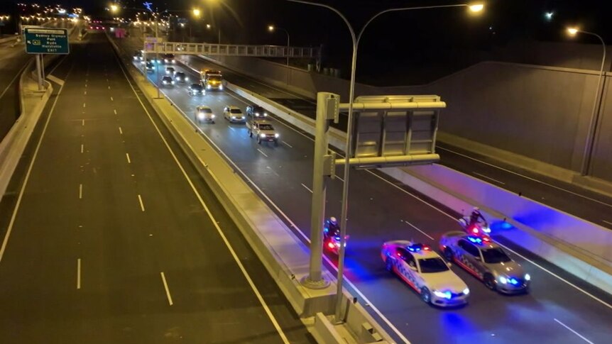 police vehicles leading a convoy of cars down a motorway