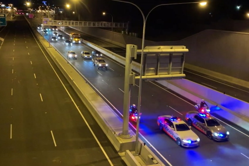 police vehicles leading a convoy of cars down a motorway