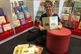 Librarian Ann-Maree Dyer sits on a library floor and is surrounded by books.