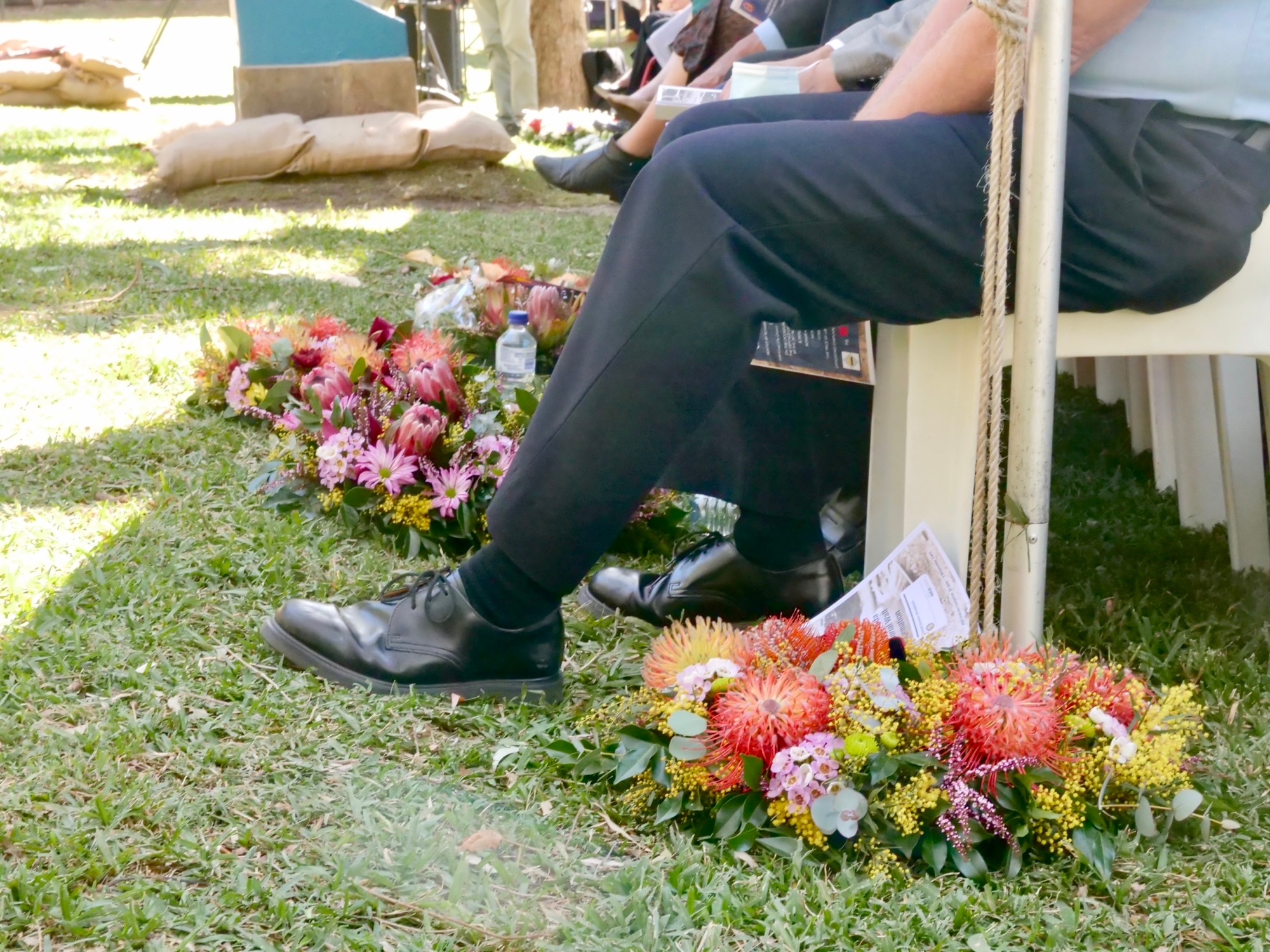 Colorful wreaths lay on the green grass next to the foot of a guest at the 80th commemorations