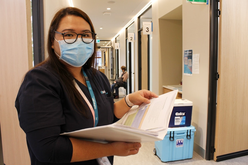 A young woman with a surgical mask and glasses looks up from a folder with two eskys in the background