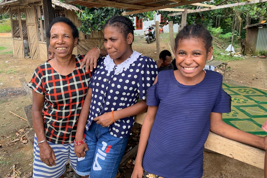 Three women lean against a bench smiling for the camera.