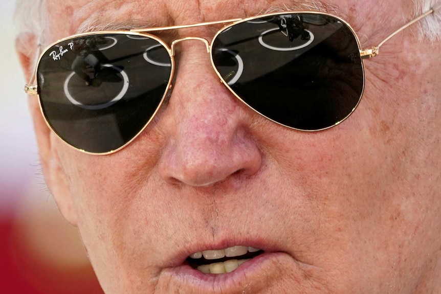Joe Biden speaks while wearing sunglasses. His face is shot in close-up
