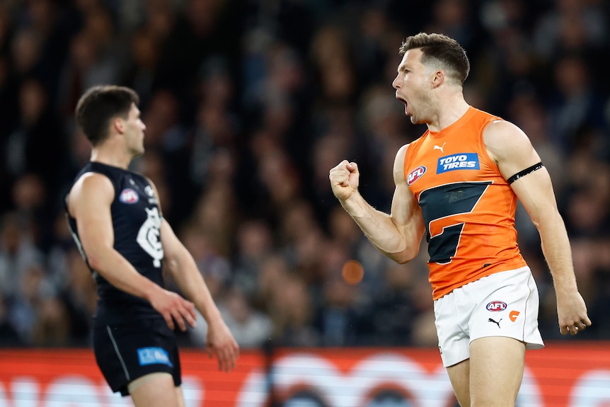 A Greater Western Sydney AFL star pumps his fist in celebration as he runs back after kicking a goal.