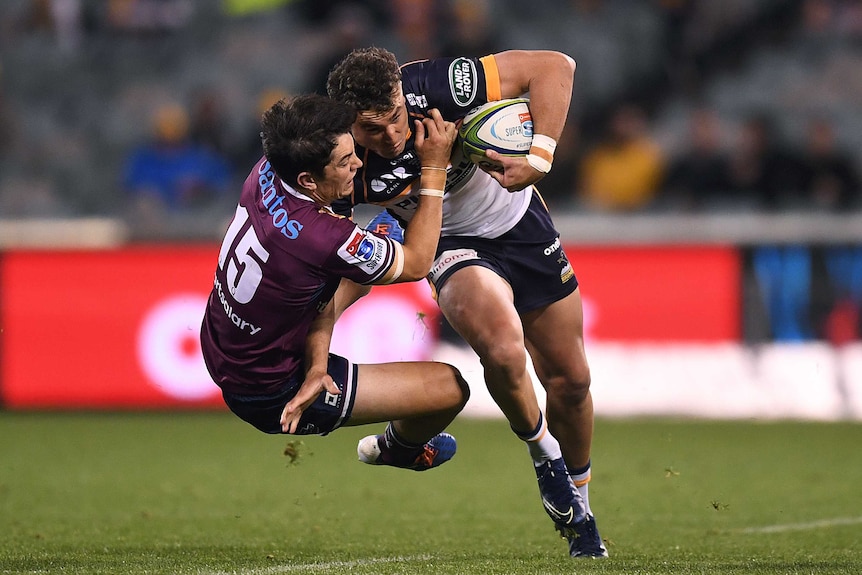 A Queensland Reds Super Rugby AU player is in mid-air as he attempts to tackle a Brumbies ball carrier.