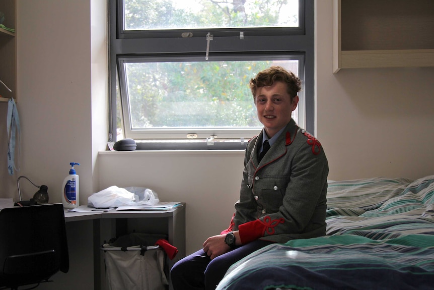 Fergus Friend sitting on a bed in the boarding house.