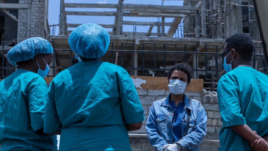 A group of health professionals in masks and scrubs stand together talking