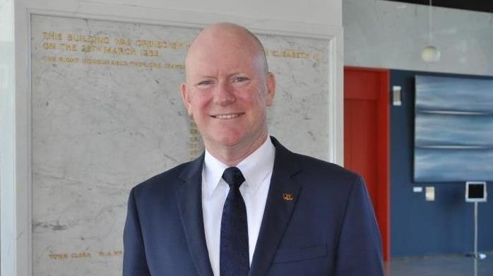 A man wearing a suit and tie smiles for the camera in the City of Perth building lobby.