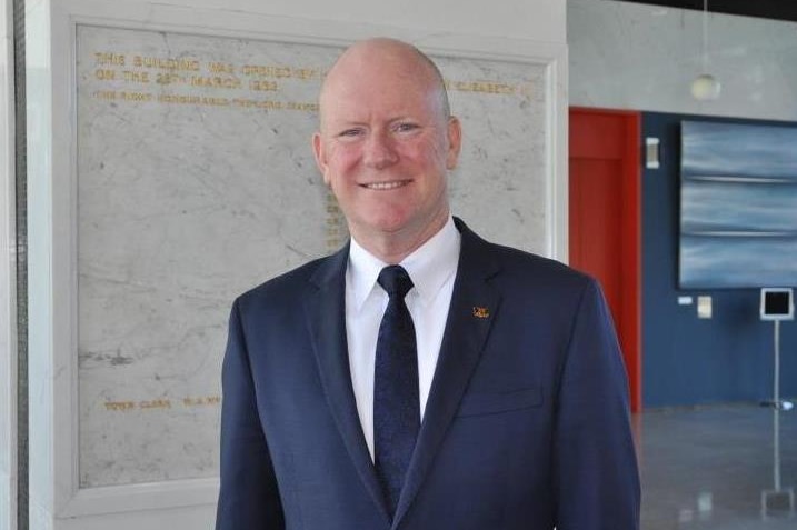 A man wearing a suit and tie smiles for the camera in the City of Perth building lobby.