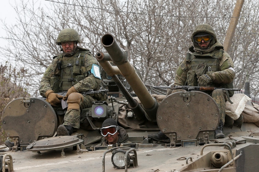 Three men in tactical gear sit on top of a Russian army tank
