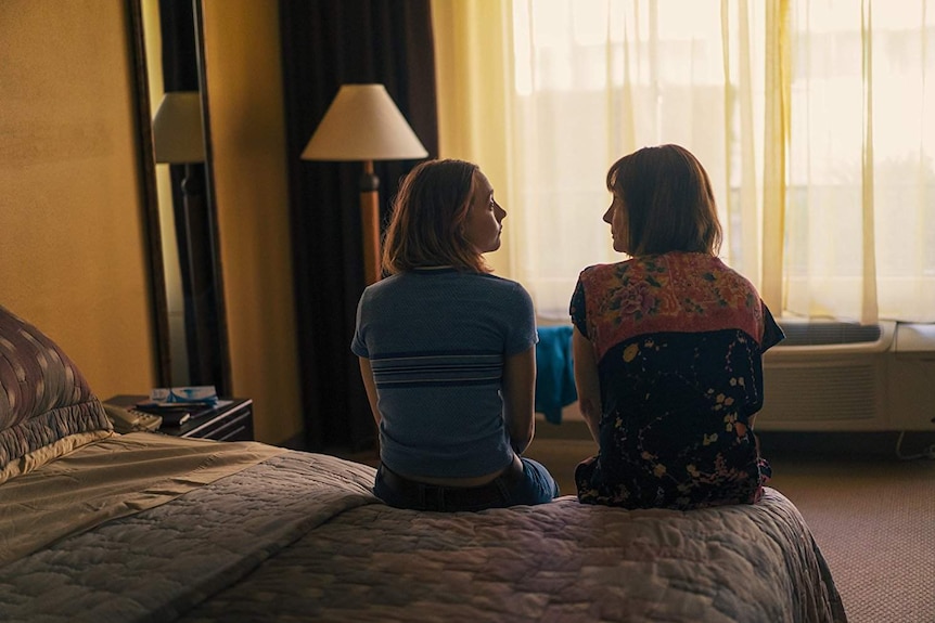 Colour still from 2017 film Ladybird of Saoirse Ronan and Laurie Metcalf sitting on a bed facing a room window.