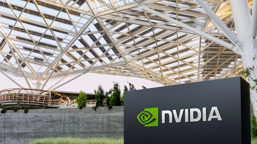 Nvidia's white and green logo is displayed on a matte-black sign outside a large, architectually complex pavilion.