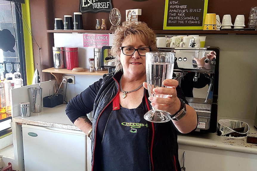 In her coffee shop Michelle Keen holds a glass of water in her left hand towards the camera.