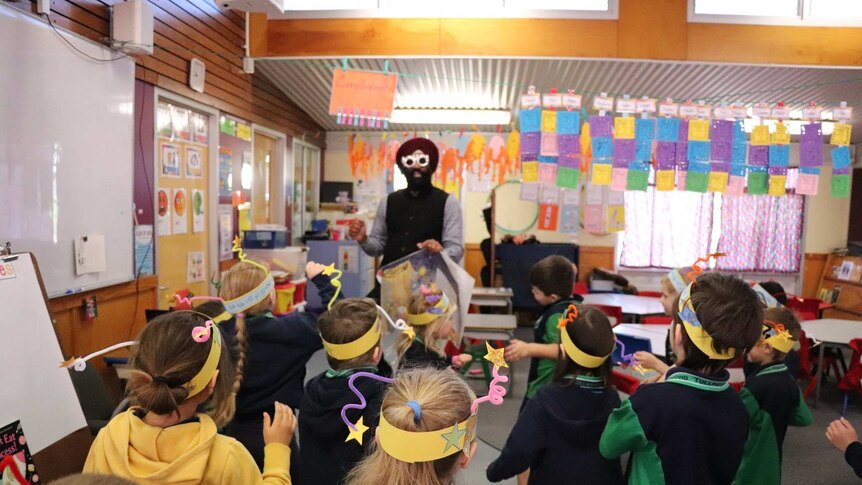 Iqbal Singh wears funny glasses and stands in front of a group of primary school students in hand-made head dresses.