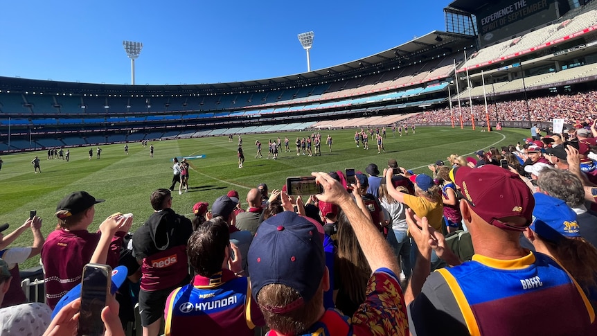 Brisbane Lions fans wear blue and maroon merch while cheering from the MCG seats