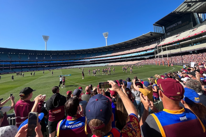 Brisbane Lions fans wear blue and maroon merch while cheering from the MCG seats