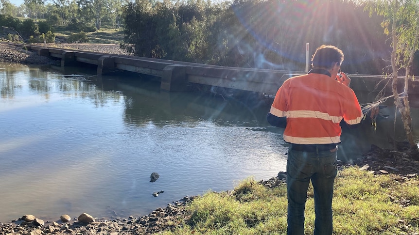 A workman clad in high-vis stands in front of a waterway.