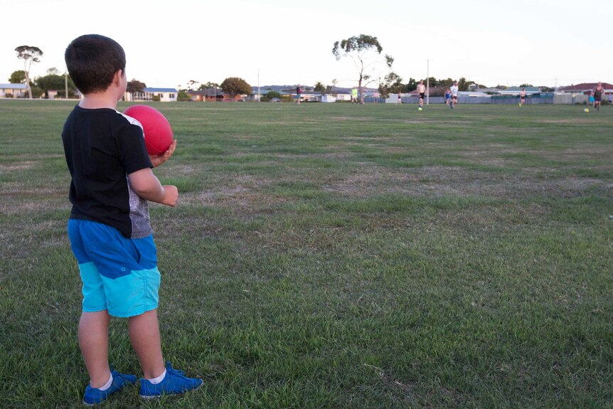 Young boy watches football team training, Tasmania.