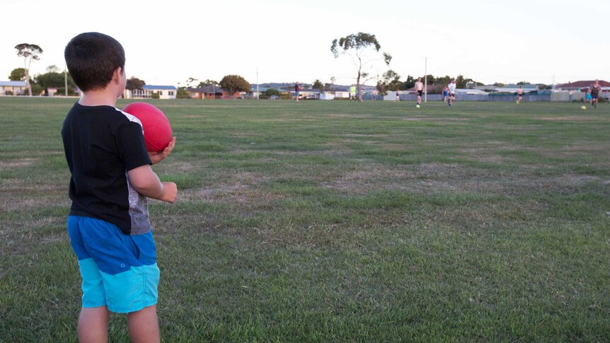 Young boy watches football team training, Tasmania.