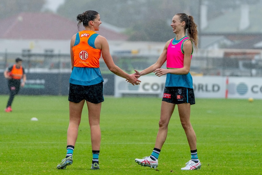 two aflw women shaking hands and smiling in the rain, in bibs