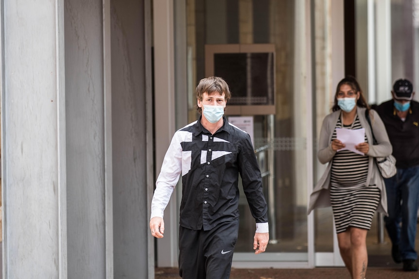 A man wearing a mask leaves a court building after being sentenced. 