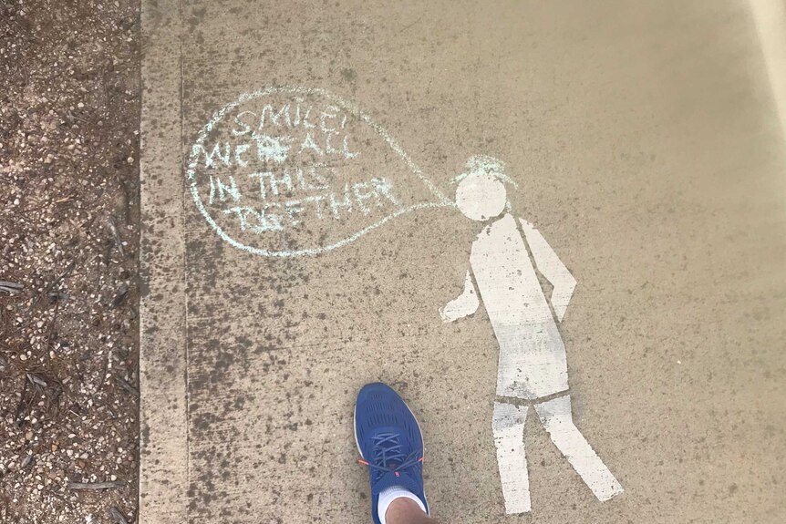 A speech bubble written in chalk on a footpath walking sign saying 'smile, we're all in this together'.
