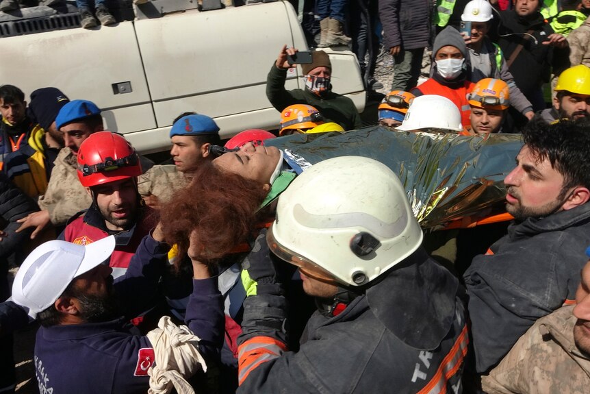 Young woman carried on stretcher through crowed.