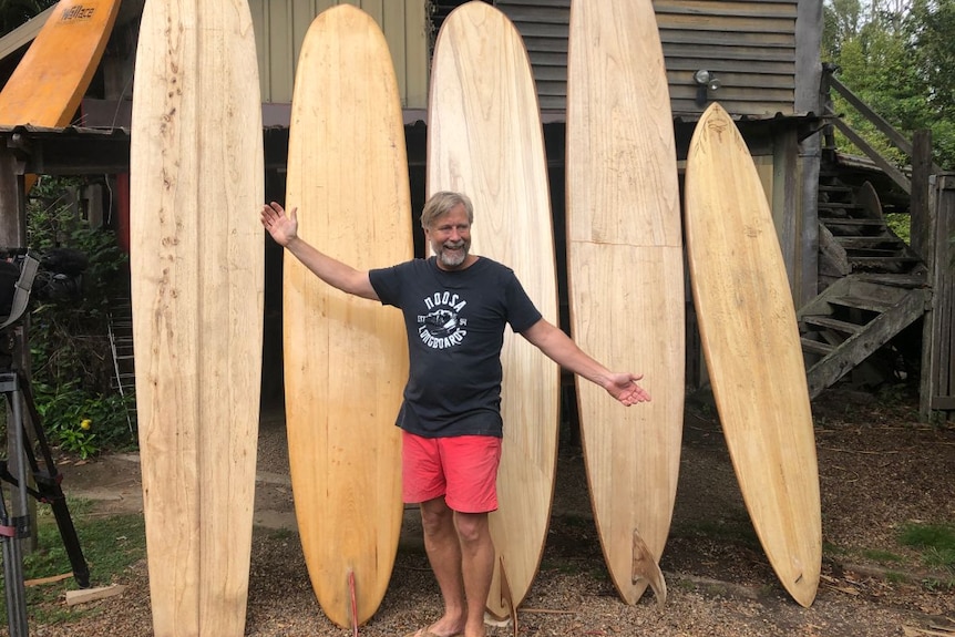 Tom Wegener stands in front of five wooden surfboards.