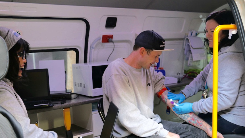 A man is treated inside a GP van by a doctor, with a nurse looking on.