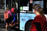 people boarding a bus, one woman wearing a mask