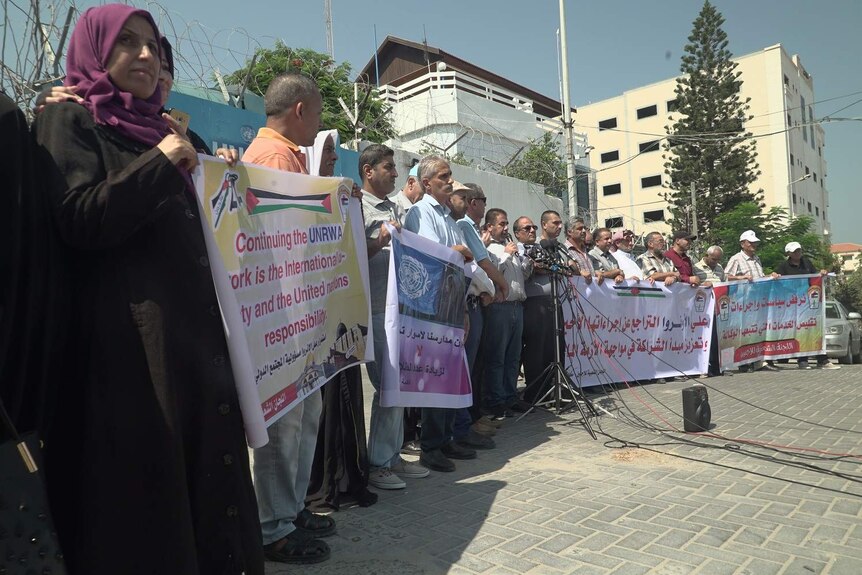 Palestinians holding banners protest in a Gaza city square.