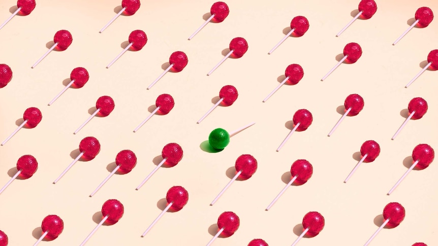 Many red lollipops facing to the right, with one green lollipop in the middle facing the left.