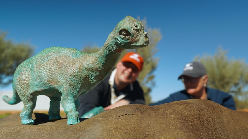 Dinosaur sculpture with two people sitting in background