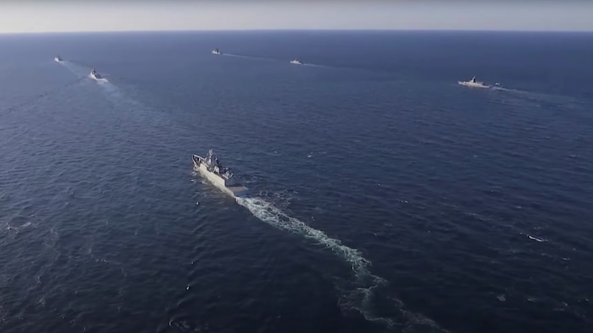 A high shot of five ships sailing away from the camera on a blue sea on a clear day