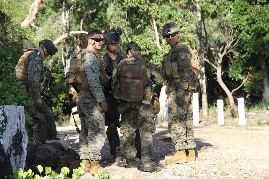4 US Marine soldier stand around surrounded by trees at an army training facility.
