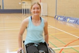A wheelchair basketball player smiles for the camera while on a basketball court.