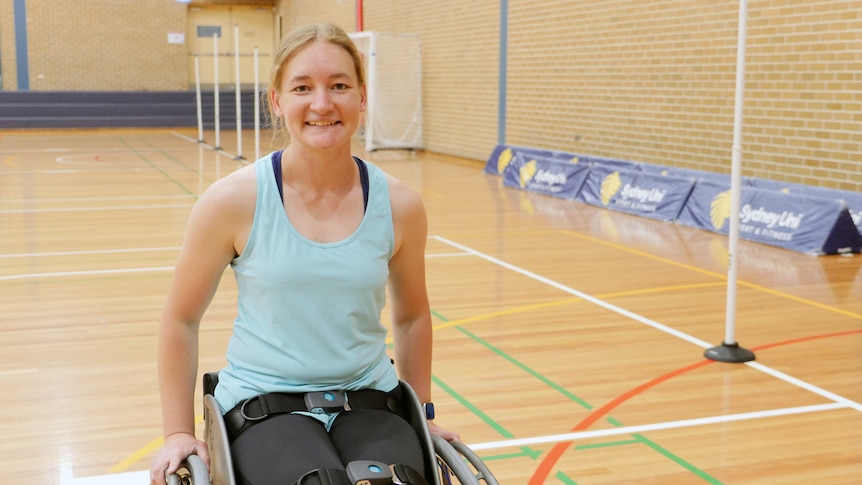 A wheelchair basketball player smiles for the camera while on a basketball court.