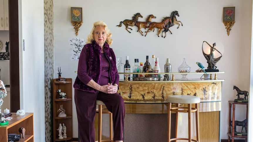 A woman sits next to a bar inside an ornately decorated home.