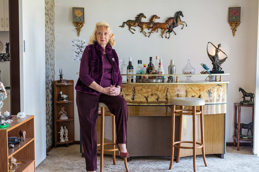 A woman sits next to a bar inside an ornately decorated home.