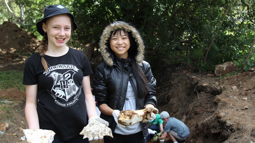 Two young girls hold pieces of dirt covered rock