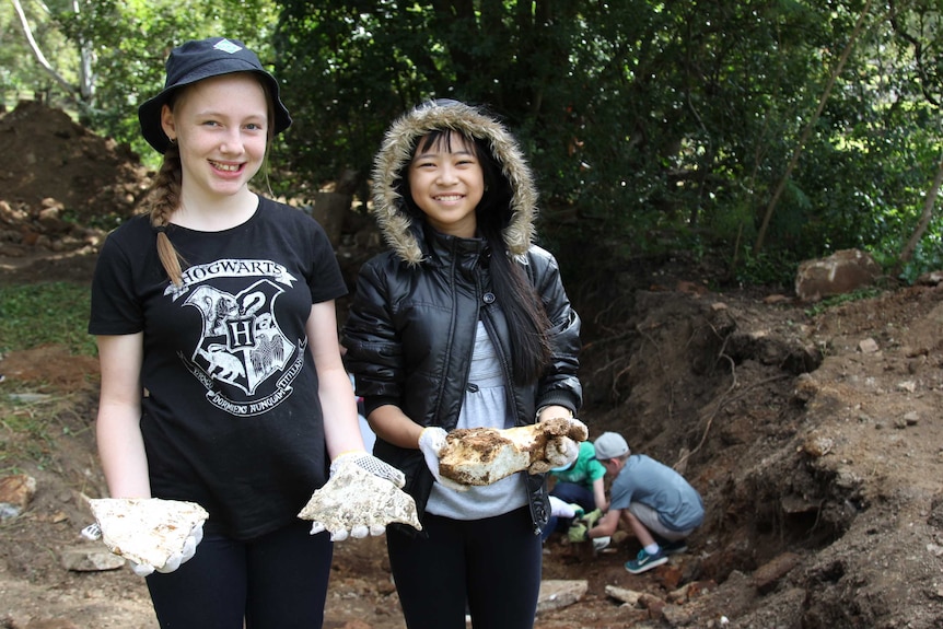 Two young girls hold pieces of dirt covered rock