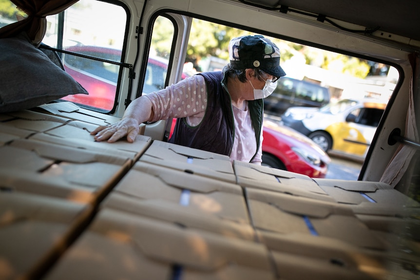 A woman wearing a mask puts a hand on boxes stacked inside a van. 