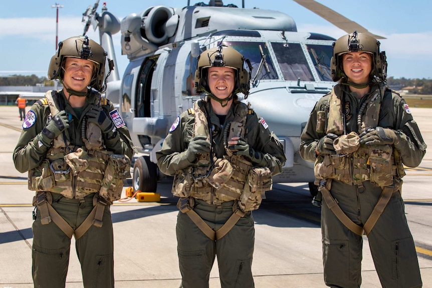 Three women in front of a helicopter.