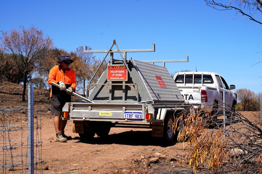 A man wearing orange loads a trailer bearing a sign saying Blazeaid at work
