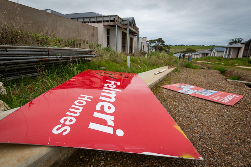 A red sign reading Felmeri Home on the ground, with construction material and houses in the background